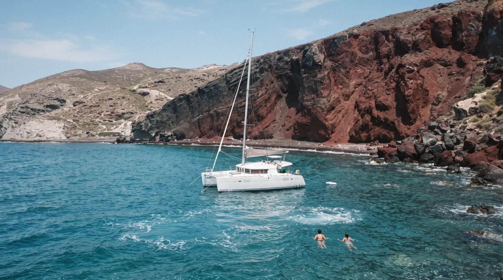 A white sailing catamaran anchored off the red cliffs of the south coast near Akrotiri at 13:00, santorini boat tour, Santorini Greece