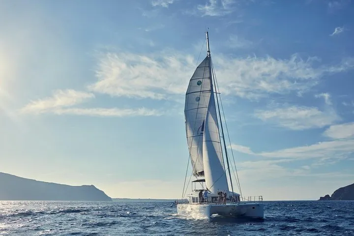 Catamaran under sail at sunset beside the caldera cliffs on a Santorini sunset sailing cruise, Santorini Greece